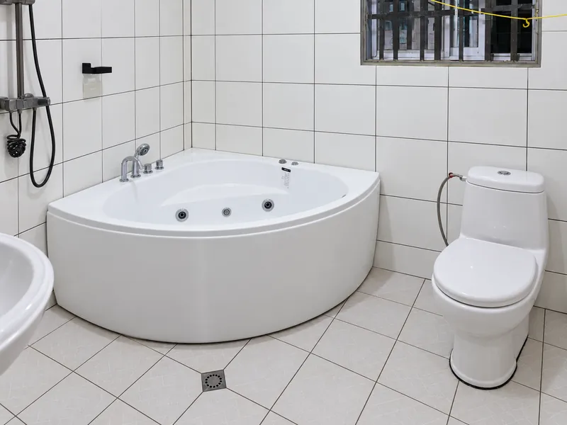 Tiled bathroom with a white corner bathtub and toilet.