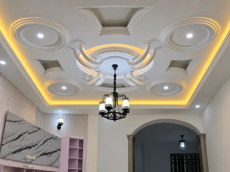 Interior with an ornate white ceiling, amber cove lighting and a black lantern chandelier.